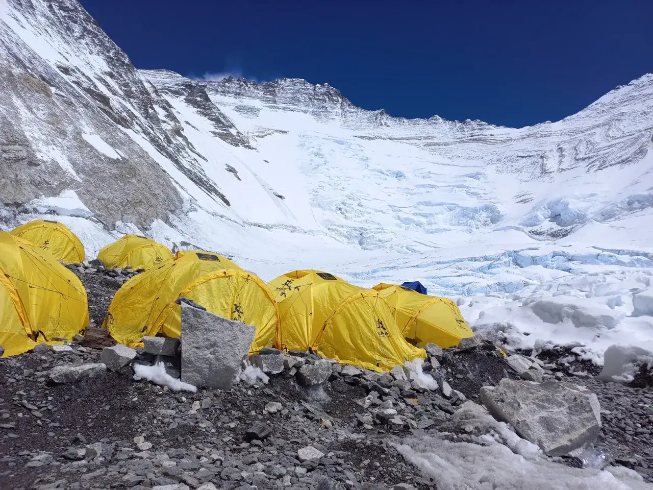 Żółte namioty obozowiska na zboczu Mount Everest, przygotowane do wejścia na szczyt. Lodowiec i skaliste podłoże.