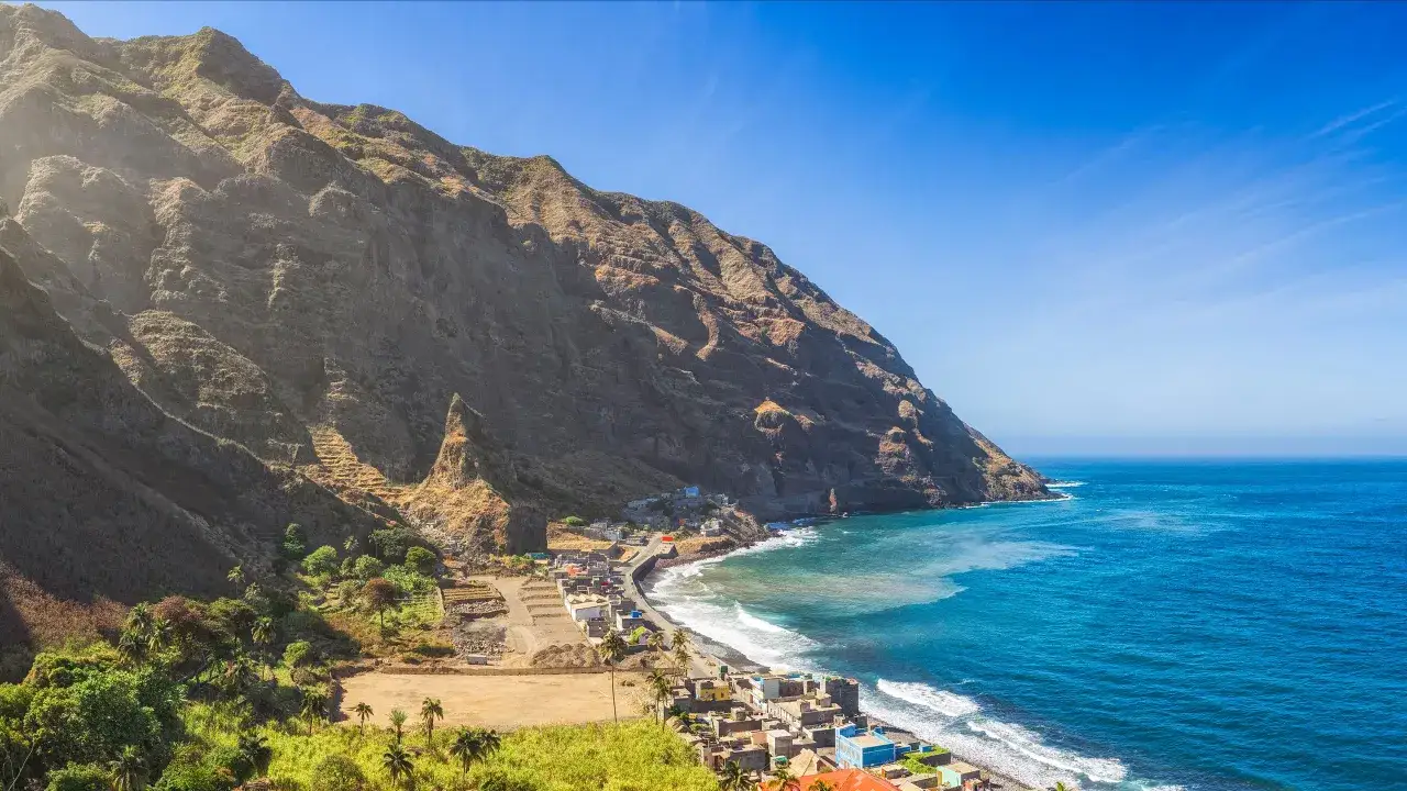 Wioska u podn&oacute;ża stromych g&oacute;r na wyspie **Cap Verde**. Turkusowe morze obmywa kamienistą plażę, a domy wtulają się w zbocza.