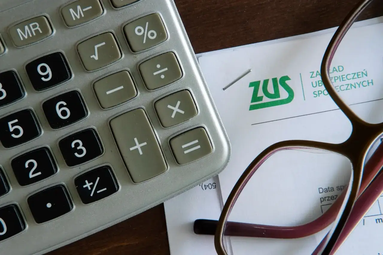 Kalkulator i dokument ZUS leżą obok okularów. Obrazek może pomóc zrozumieć, co to jest renta rodzinna i jak ją obliczyć.