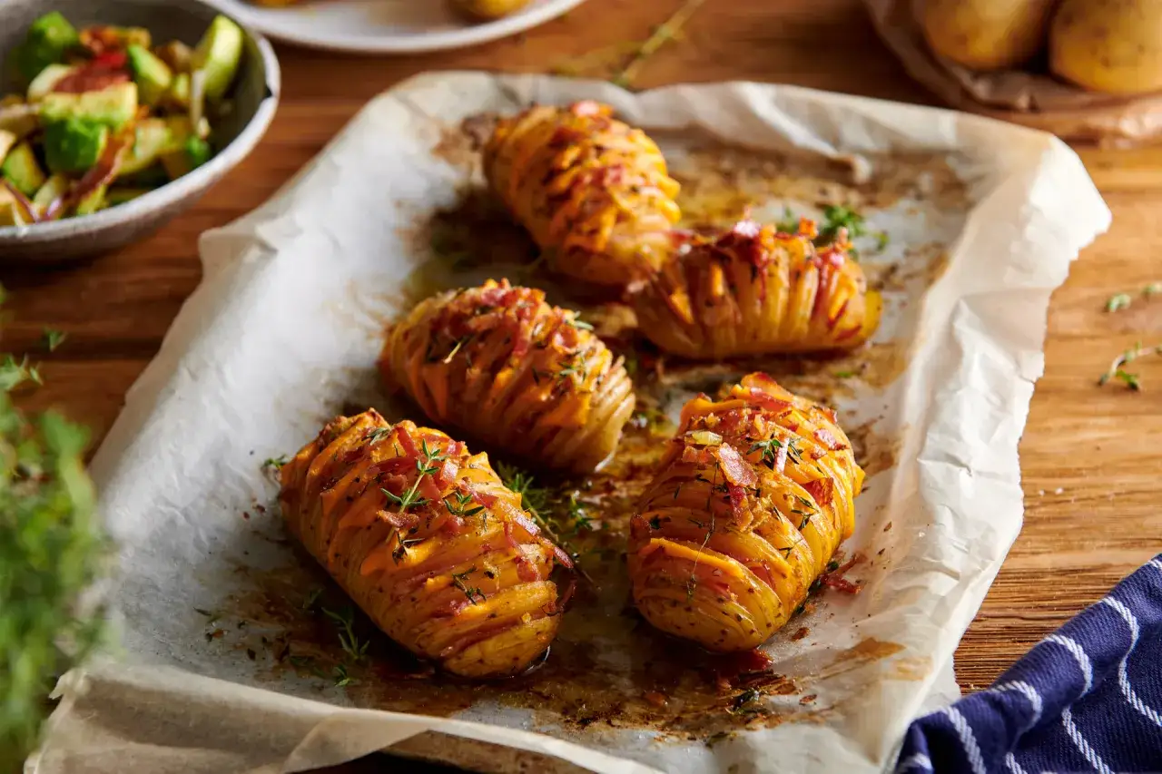 Ziemniaki zapiekane w piekarniku, nacięte i nadziane serem i boczkiem, posypane ziołami.