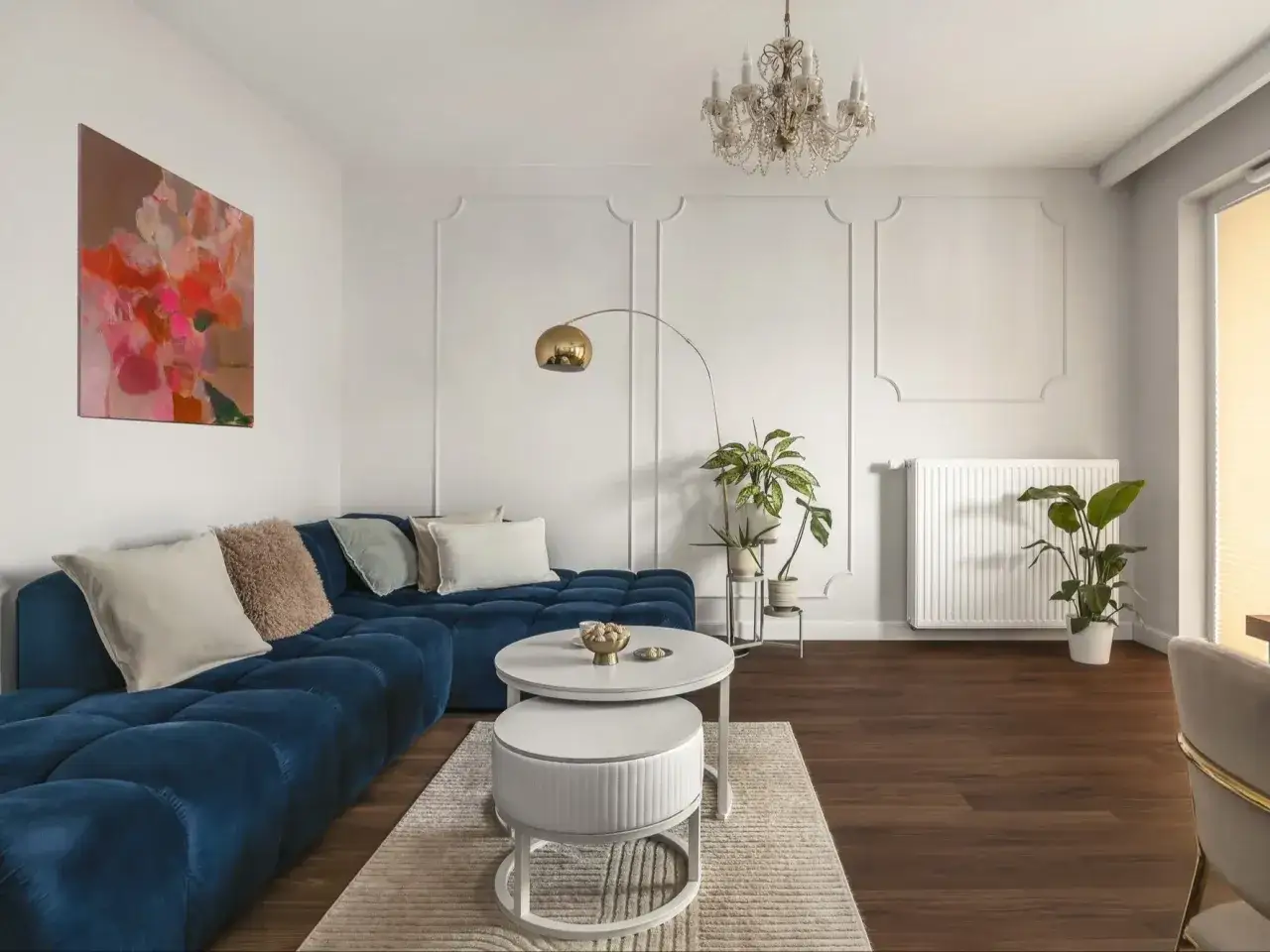 Elegancki salon w stylu paryskim z granatową sofą, sztukaterią na ścianach i kryształowym żyrandolem.