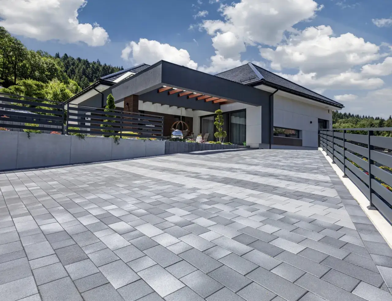 Nowoczesny podjazd z szarej kostki brukowej przed domem z drewnianą pergolą.
