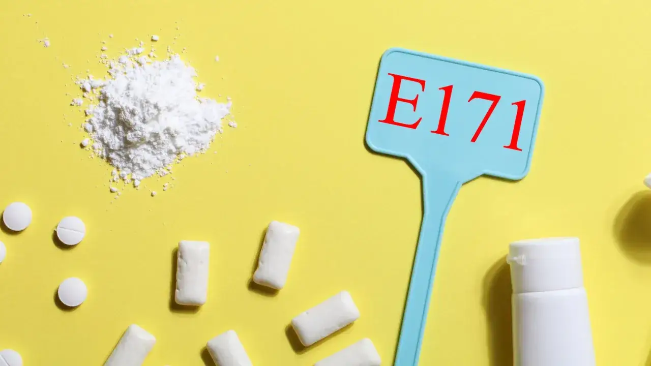 Biały proszek, tabletki i gumy do żucia na ż&oacute;łtym tle. Tabliczka z napisem E171, kt&oacute;ra odpowiada na pytanie: titanium dioxide co to jest?