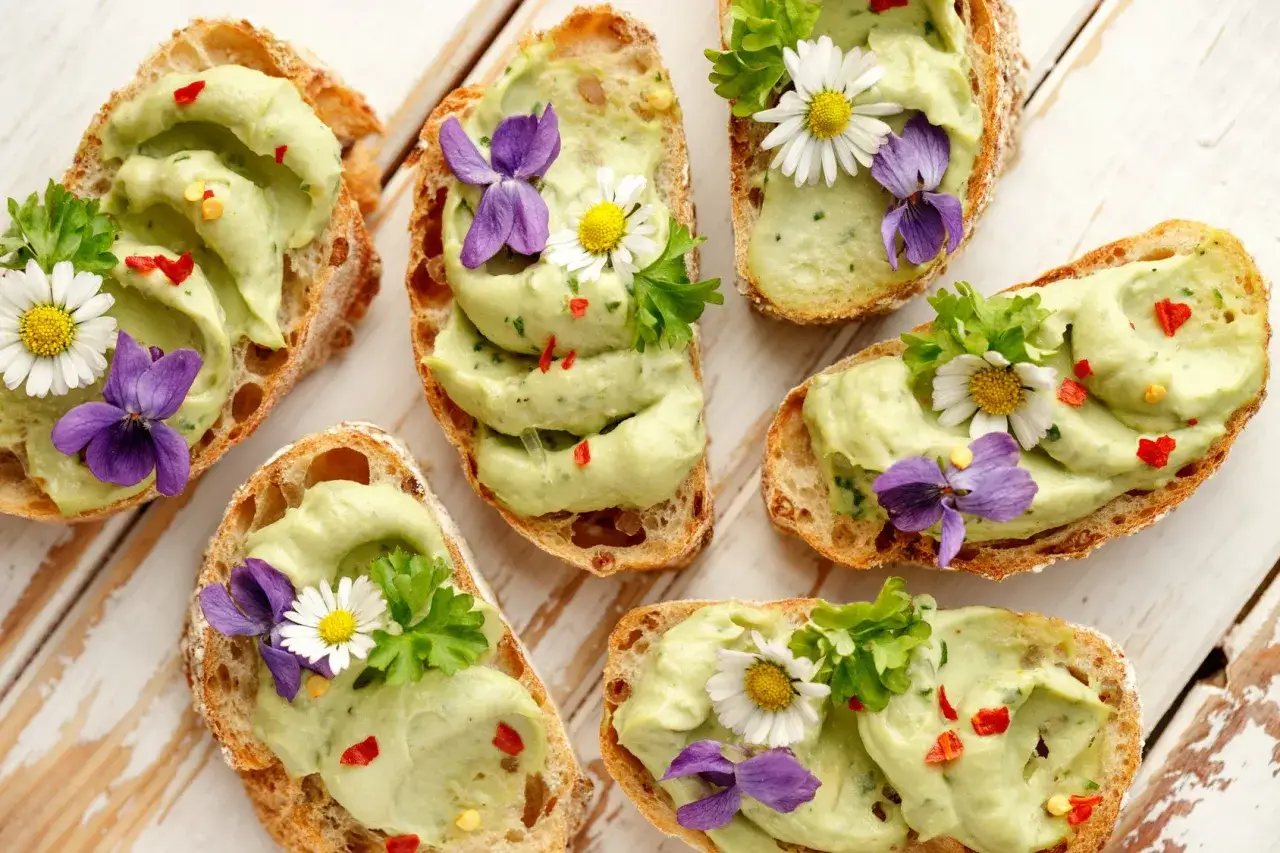 Wykwintne przystawki finger food: grzanki z pastą z awokado, ozdobione kwiatami i ziołami. Idealne na przyjęcie.