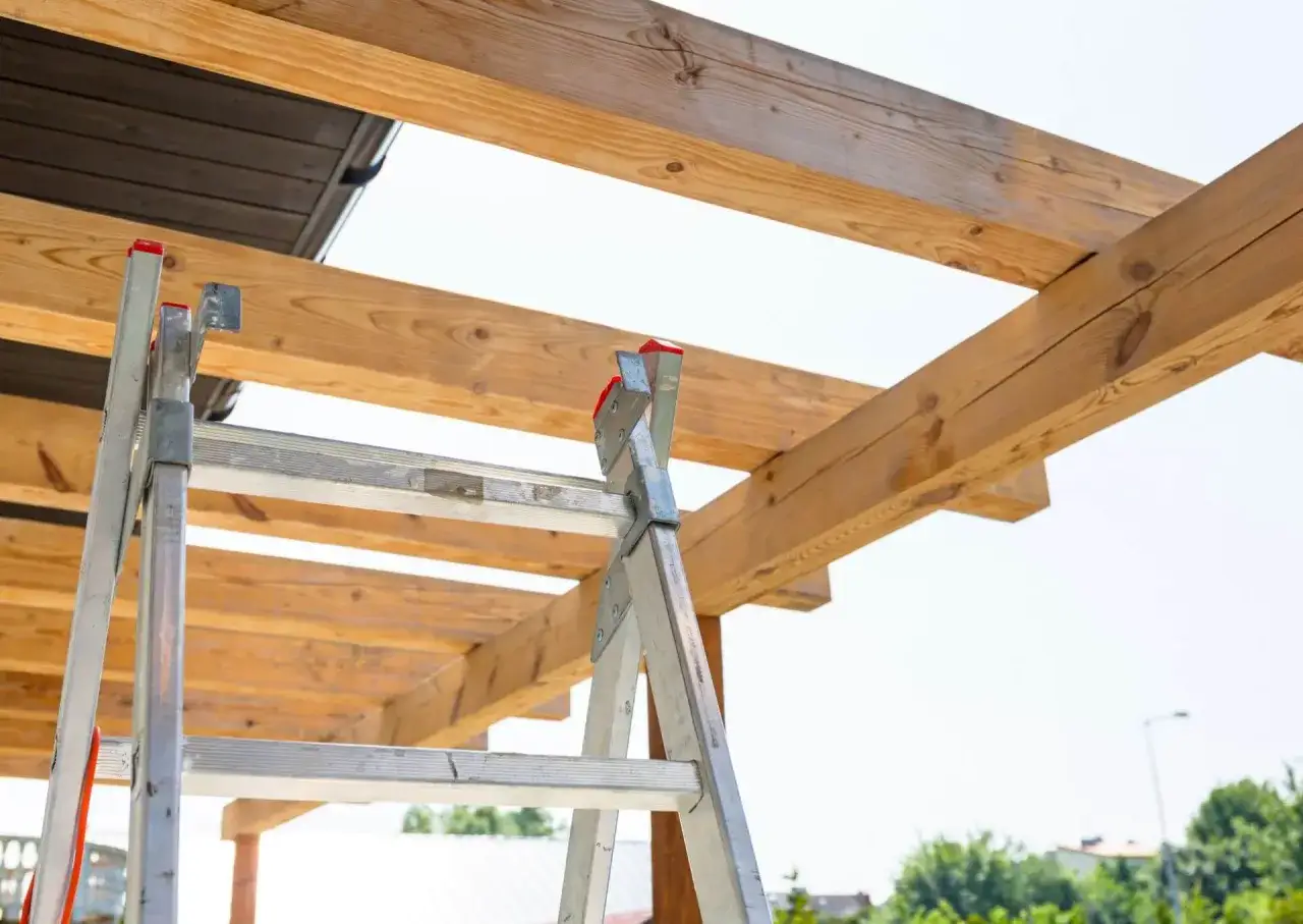 Drabina przy drewnianej konstrukcji, kt&oacute;ra będzie przedłużeniem dachu nad tarasem.