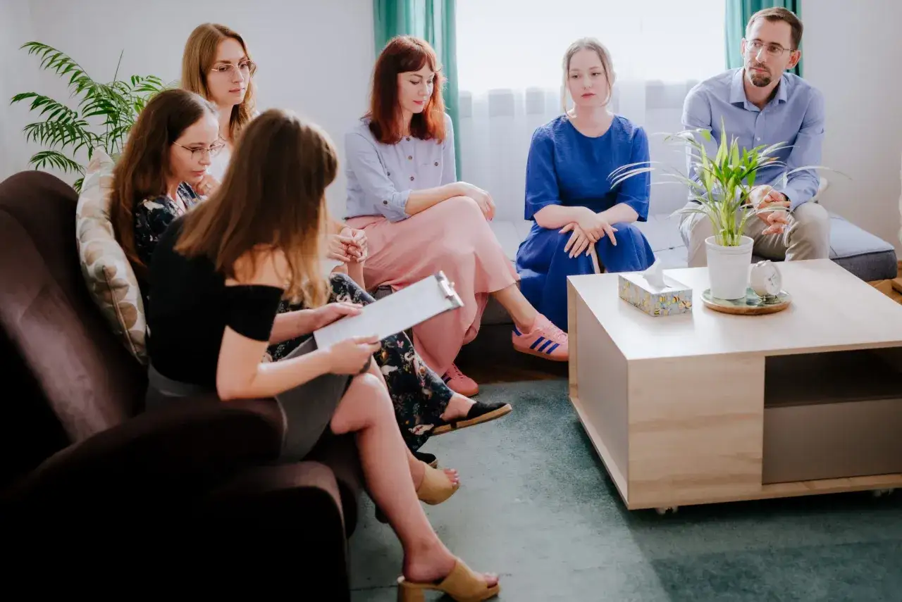 Grupa osób na sesji terapeutycznej. Kto to psychoterapeuta? To on, siedzący po prawej, prowadzi rozmowę.