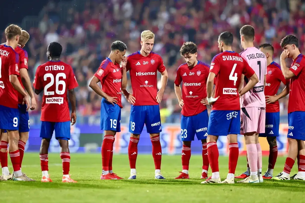 Zawodnicy Rakowa Częstochowa w czerwonych strojach, z numerami na plecach, stoją na murawie.