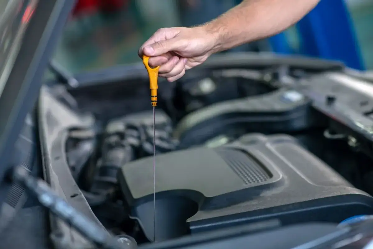 Sprawdzanie poziomu oleju w silniku. Dłoń trzymająca żółtą miarkę, która pomoże określić, ile wlać oleju do silnika.