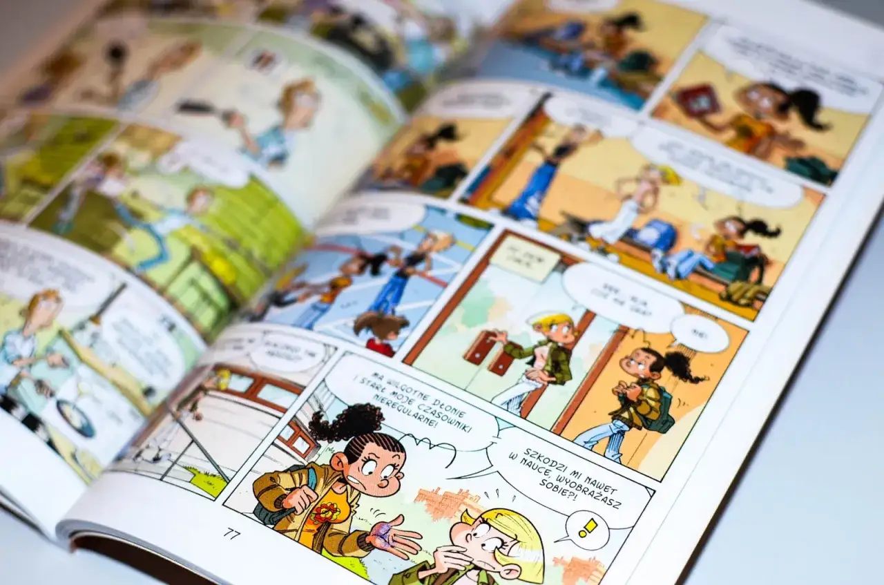 Otwarta książka z kolorowym komiksem do nauki czytania. Dwie dziewczynki rozmawiają, jedna z nich ma mokre dłonie.
