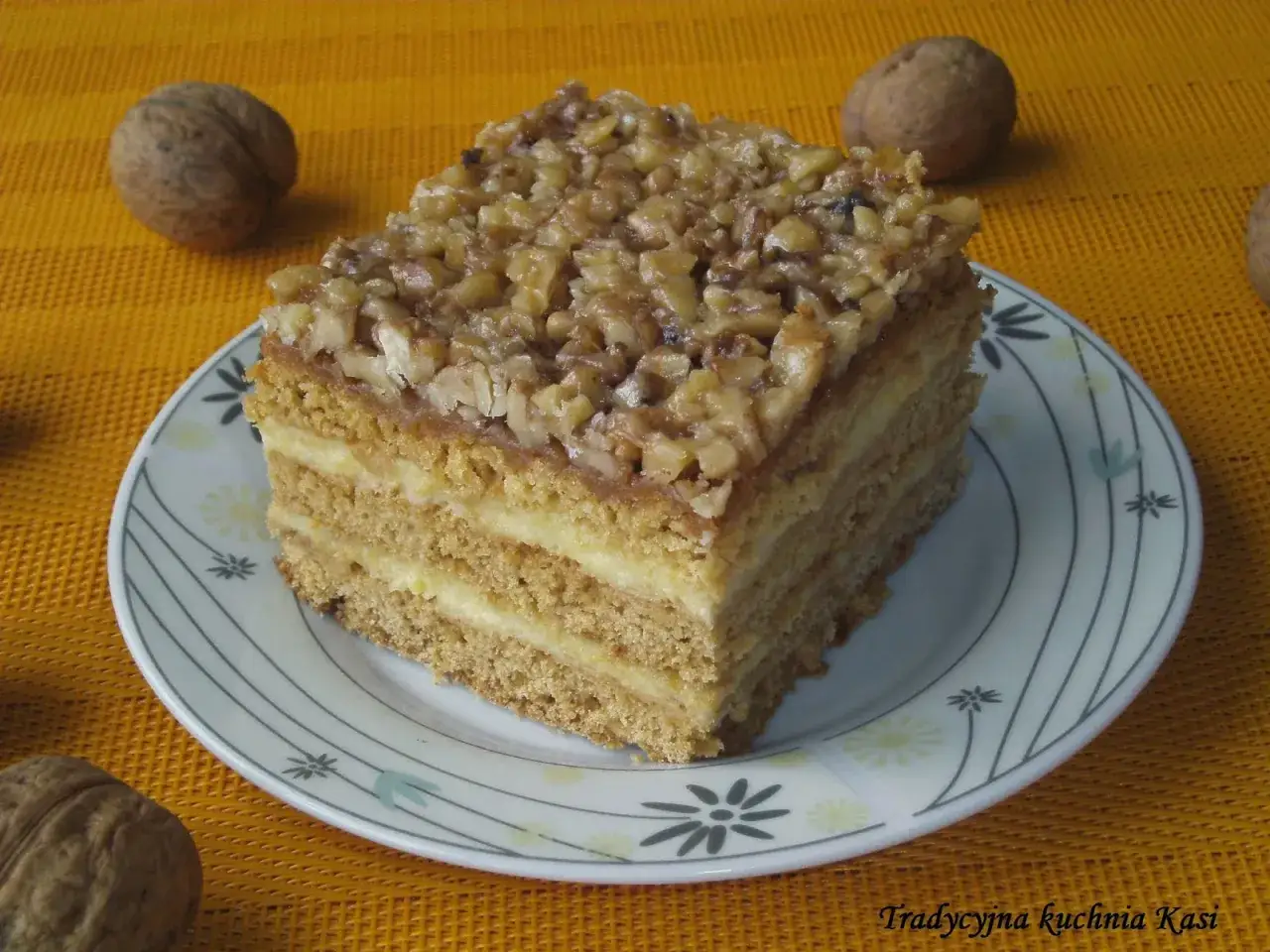 Pyszny miodownik z orzechami, przekładany kremem, na talerzyku z kwiatowym wzorem.