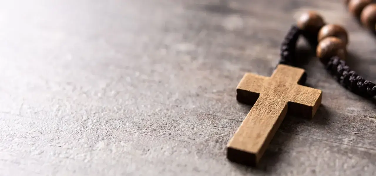 Drewniany krzyż i paciorki różańca na kamiennym tle, symbolizujące tajemnice bolesne rozważania biblijne.