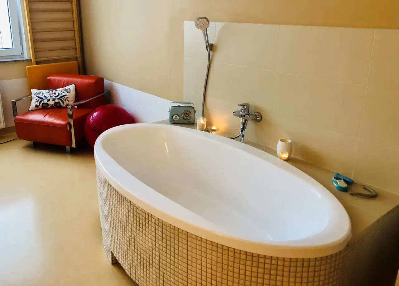 Relaksacyjna wanna i fotel w pokoju porodowym. Ciepłe światło świec i muzyka z radia mogą pom&oacute;c, jak złagodzić skurcze porodowe.