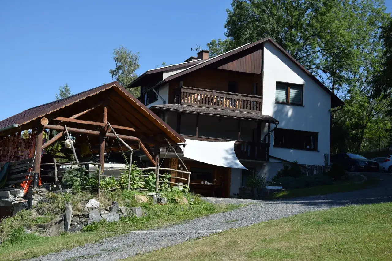 Agroturystyka bac&oacute;wka Giemzik&oacute;w to urokliwe miejsce z drewnianą wiatą i domem z balkonem, otoczone zielenią.