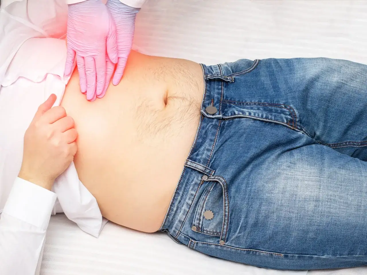 Lekarz w różowych rękawiczkach bada brzuch pacjenta, szukając gdzie jest śledziona.