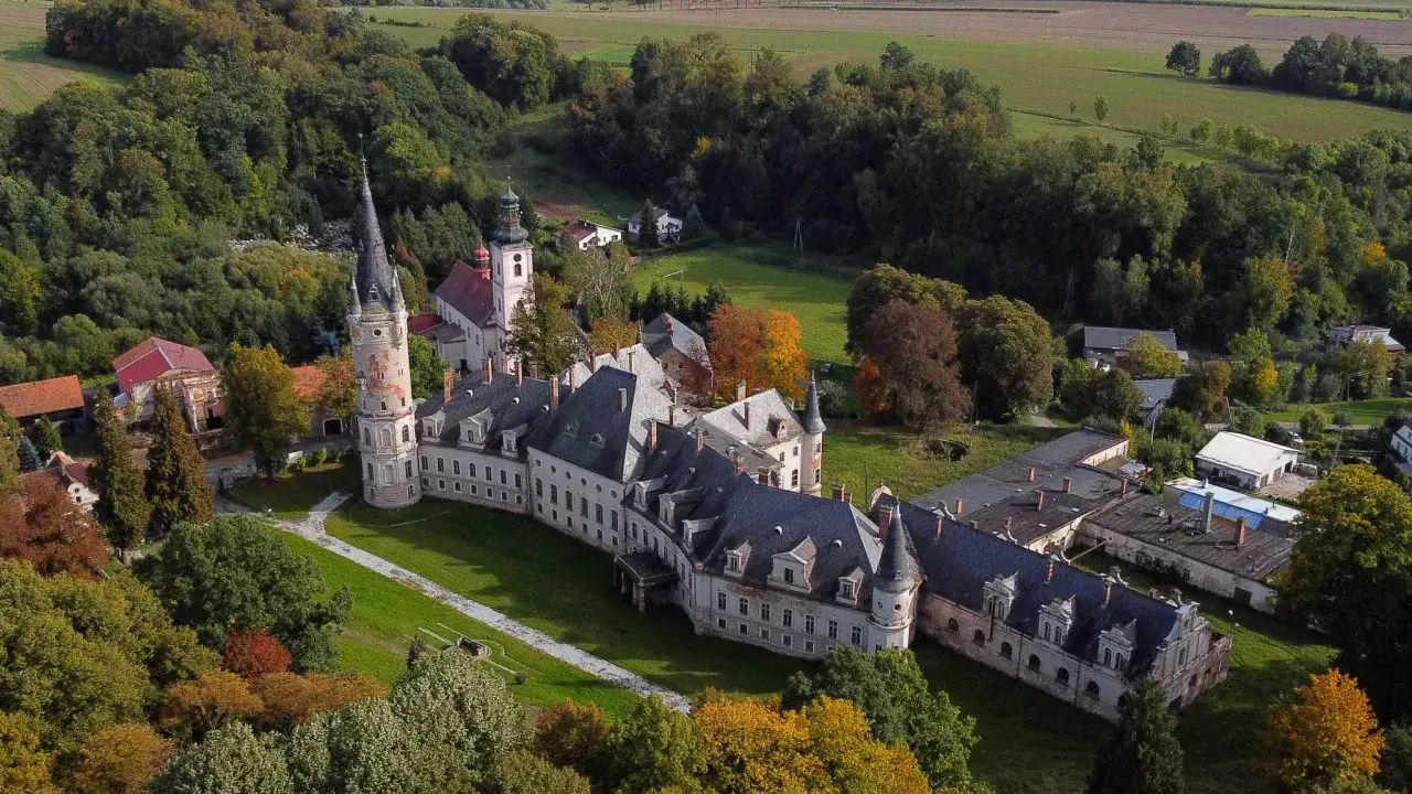 Zamek Bożków, rozległy zespół pałacowy z wieżą, otoczony jesiennym parkiem i polami.