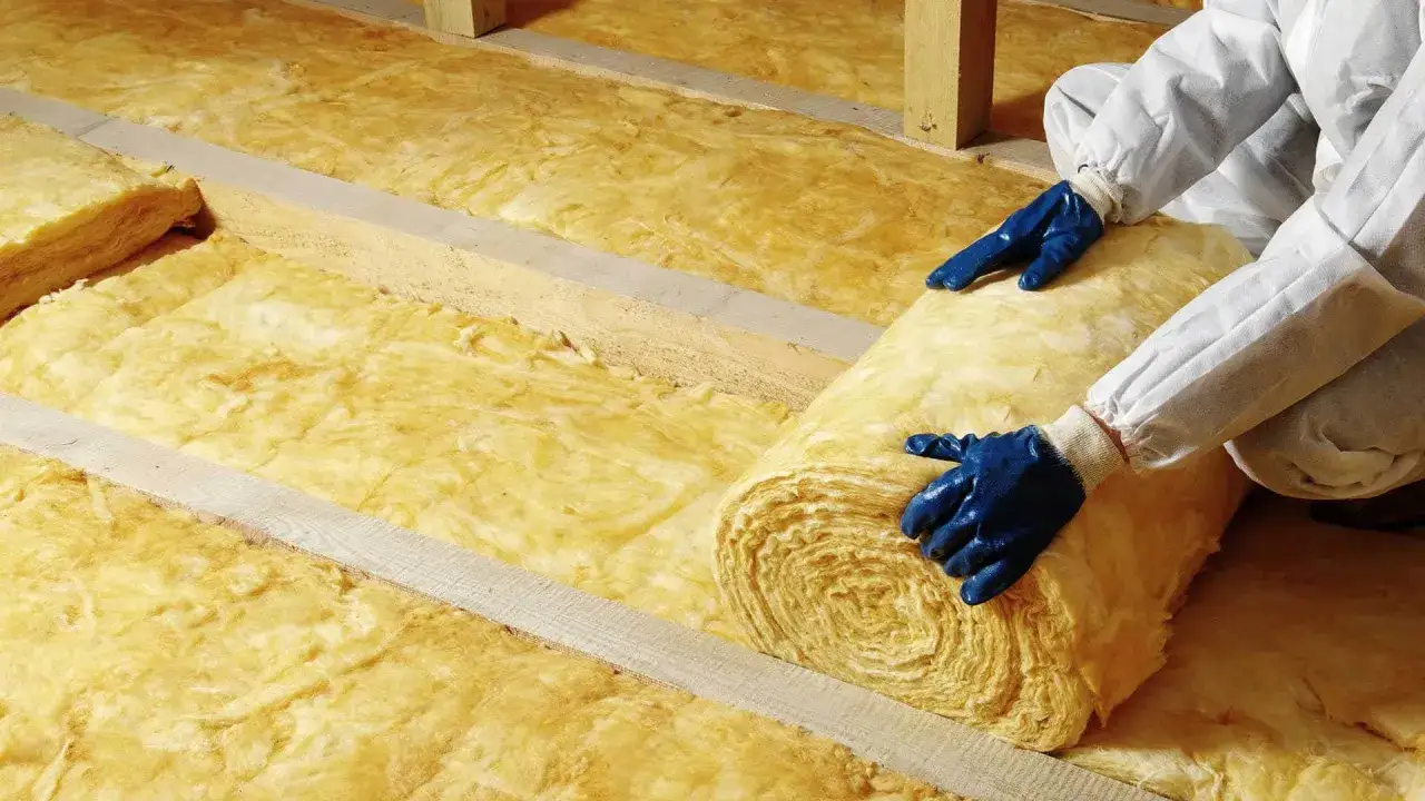 Osoba w rękawiczkach układa wełnę mineralną. To materiał izolacyjny, który można dodatkowo zabezpieczyć klejem do wełny mineralnej.