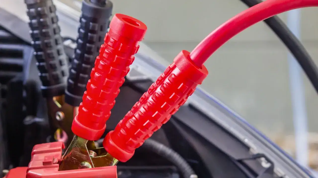 Czerwone i czarne kable rozruchowe podłączone do akumulatora. Zbliżenie na zaciski, kluczowe do tego, jak odpalić samochód na kable.