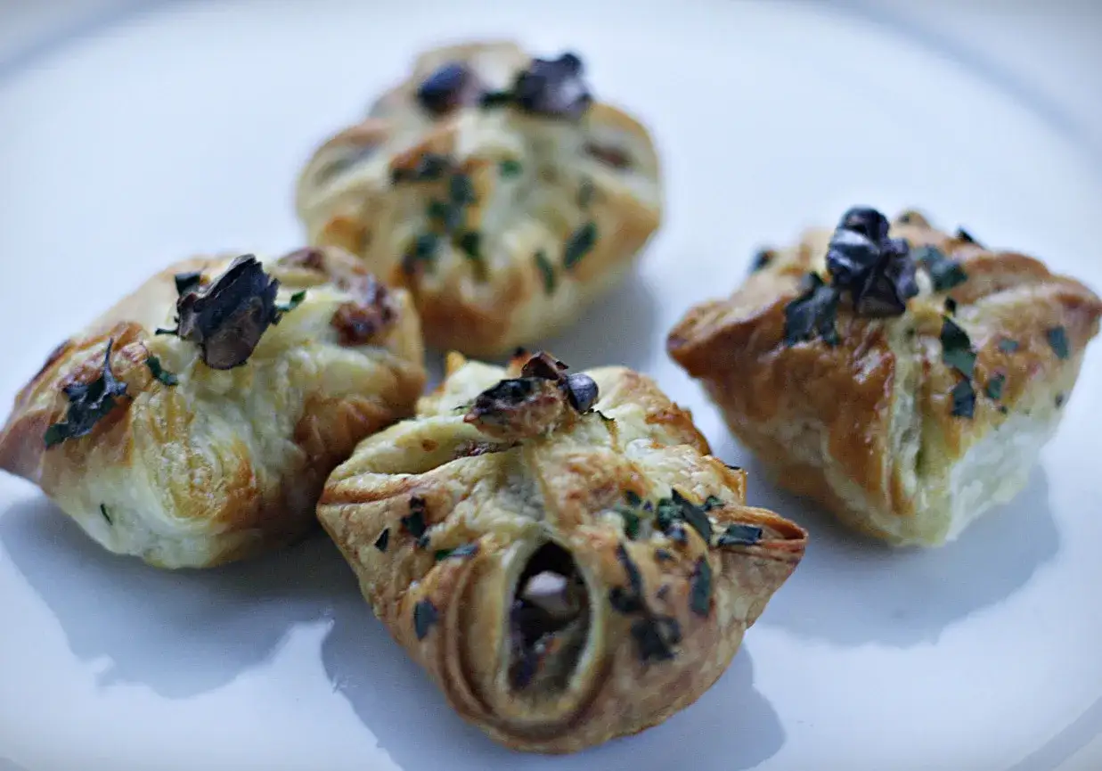 Cztery złociste sakiewki z ciasta francuskiego, ozdobione ziołami i grzybami, kuszą swoim wyglądem.