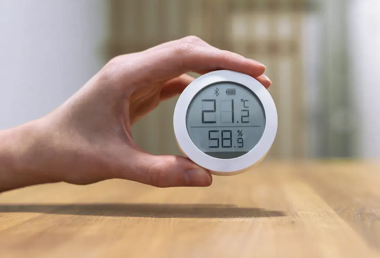 Dłoń trzyma okrągły termohigrometr, który pokazuje 21.2°C i 58.9% wilgotności. Ta jednostka wilgotności powietrza pomaga dbać o komfort.