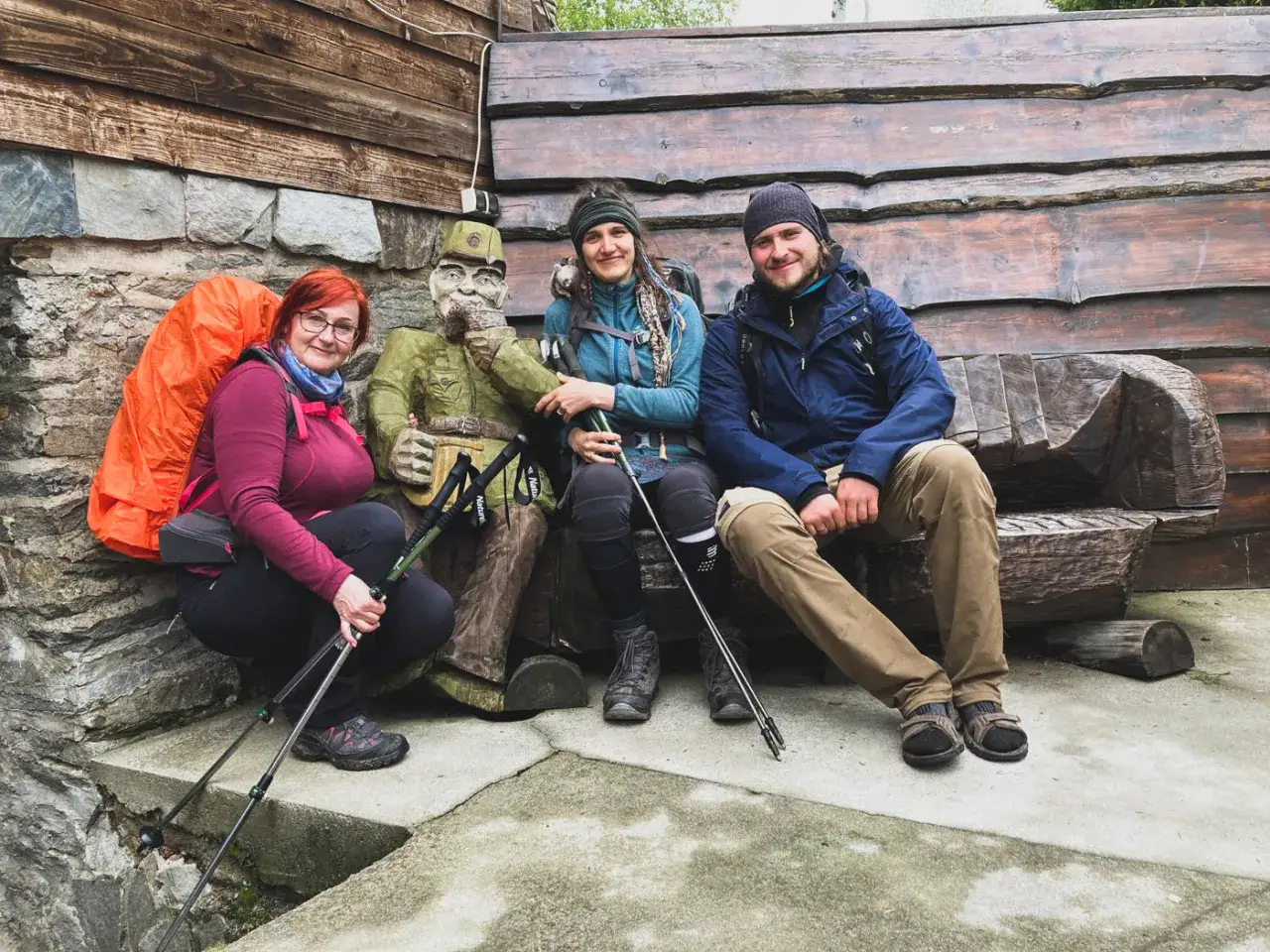 Trzy osoby z plecakami i kijkami trekkingowymi pozują z rzeźbą. Planują przejść główny szlak sudecki w kilka dni.
