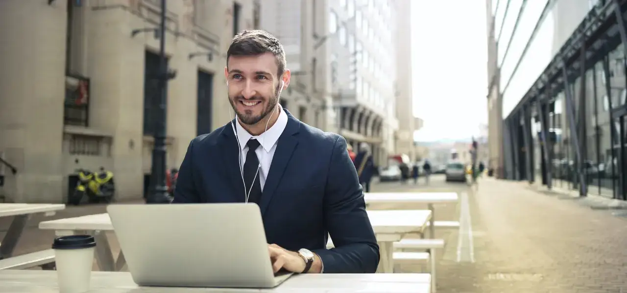 Uśmiechnięty mężczyzna w garniturze pracuje na laptopie na zewnątrz, zastanawiając się, czy darmowe treści celebryty są lepsze niż jego płatny kurs premium.