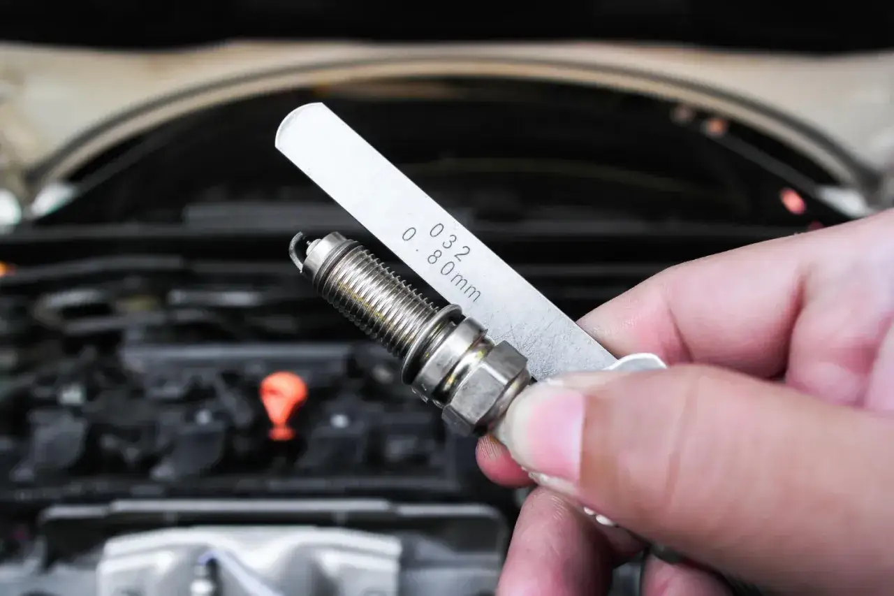 Dłoń trzyma świecę żarową i szczelinomierz. Widać jej urwany elektrod.