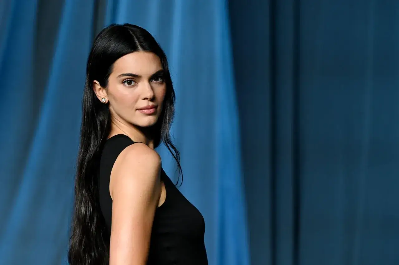 Kendall Jenner, której wiek jest często przedmiotem dyskusji, prezentuje się zjawiskowo w czarnej sukience na tle niebieskiej tkaniny.