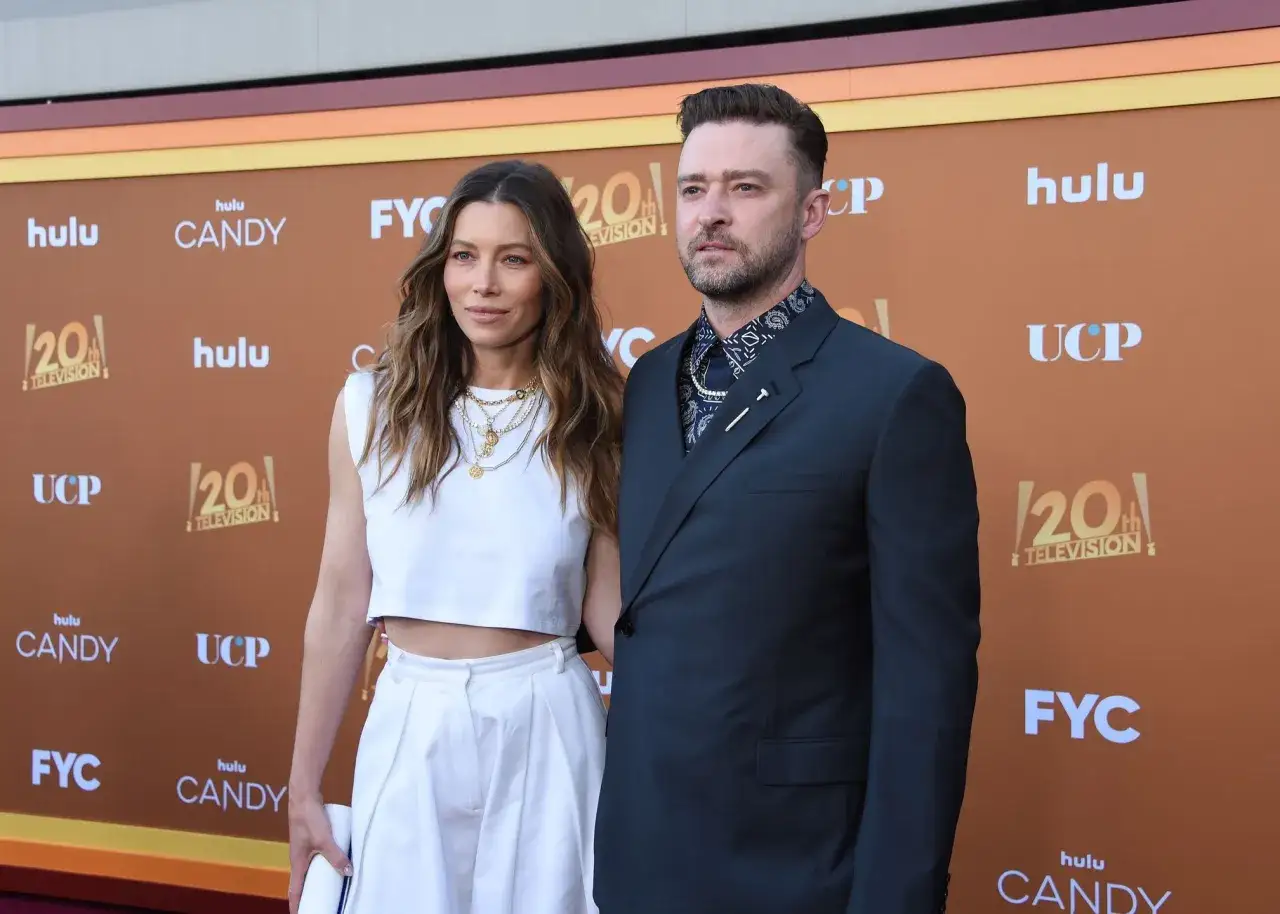 Jessica Biel i Justin Timberlake na ściance. Ona w białym topie i szerokich spodniach, on w granatowej marynarce.