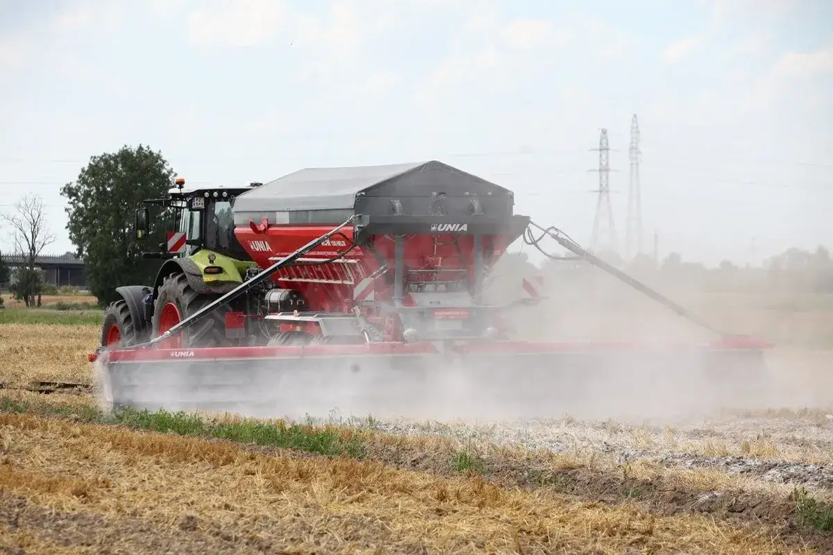 Traktor z rozsiewaczem rozsypuje wapno do ziemi na polu.