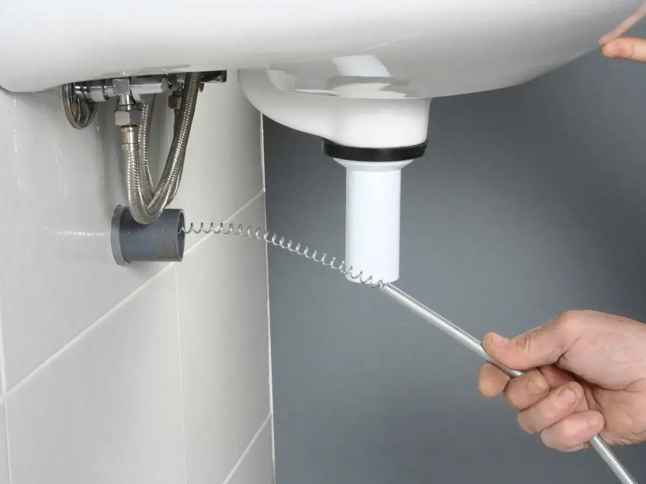 Ręka wsuwa sprężynę do rury odpływowej, by udrożnić zapchany odpływ w kabinie prysznicowej.