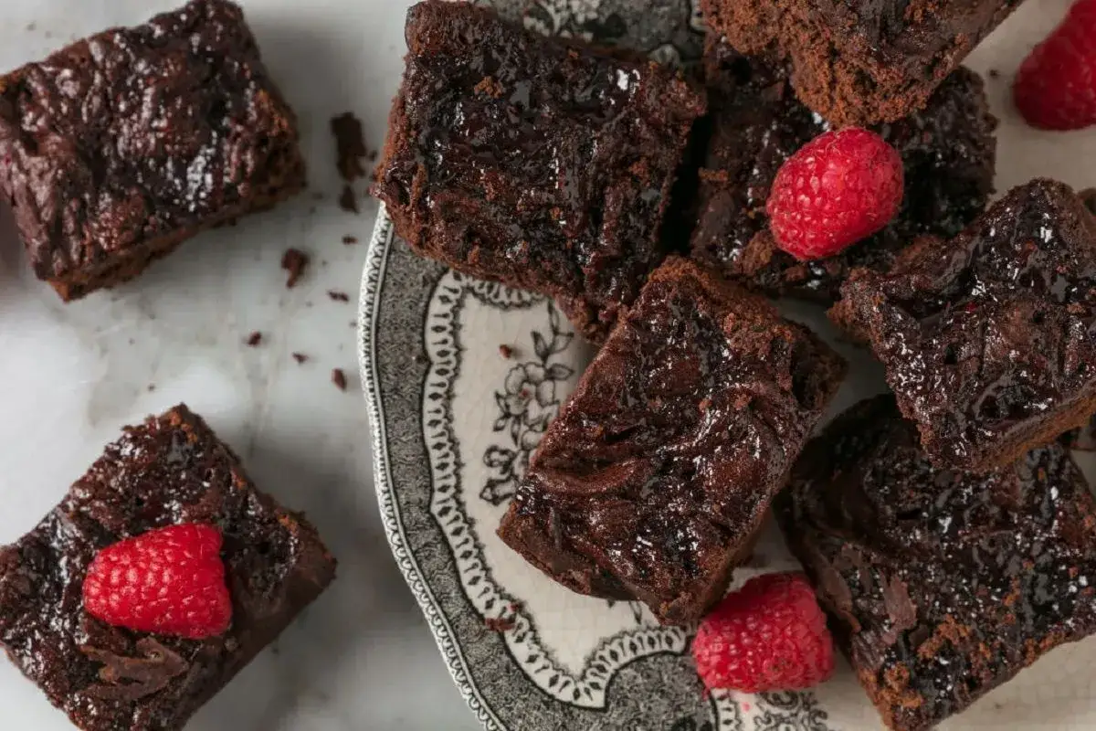 Pyszne brownie bez jajek, błyszczące od polewy, ozdobione malinami. Idealne na deser.