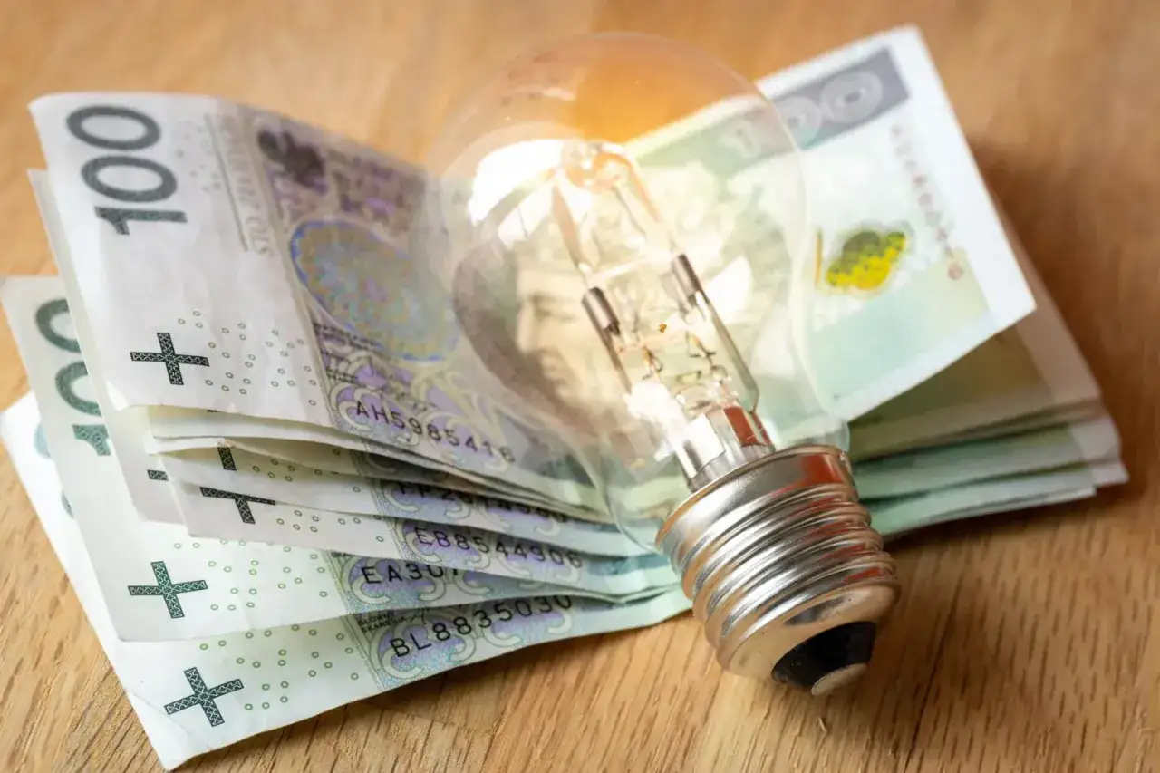 Żarówka na stosie banknotów 100 zł. Symbolizuje ulgę na prąd i rosnące koszty energii.