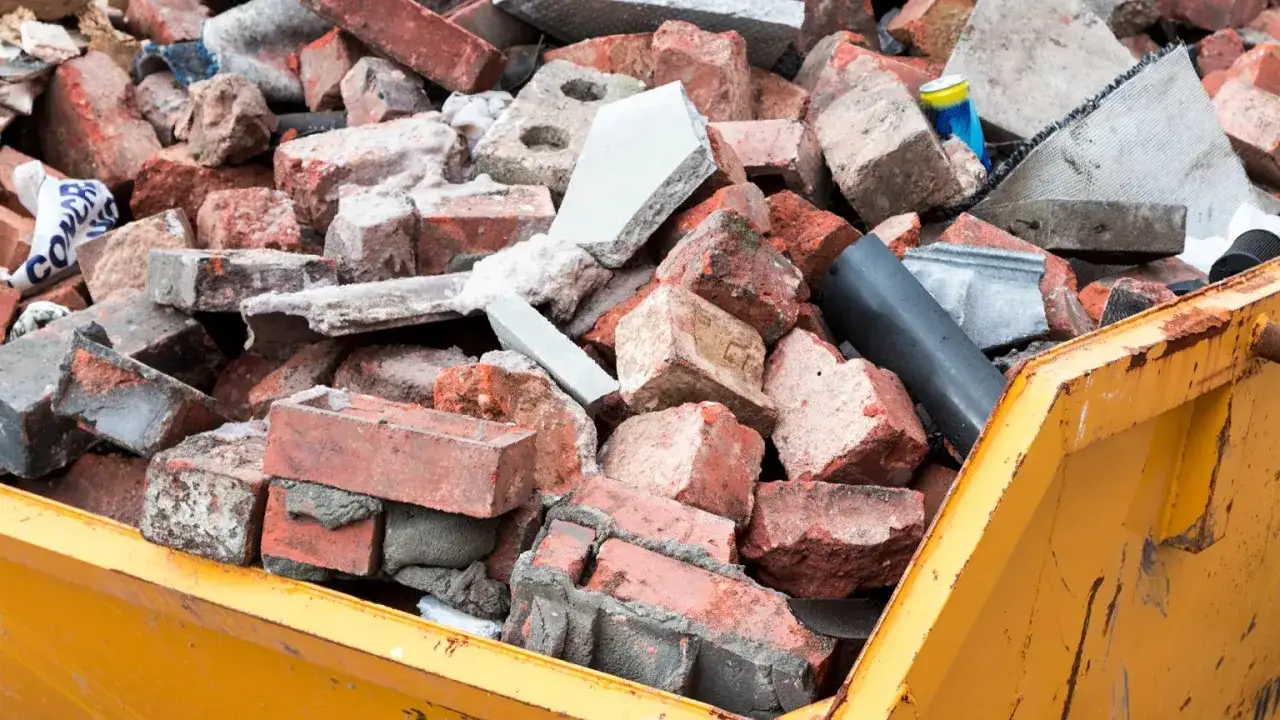 Kontener z gruzem budowlanym, w tym cegłami i fragmentami betonu. Tu dowiesz się, gdzie wyrzucać kafelki i inne odpady budowlane.