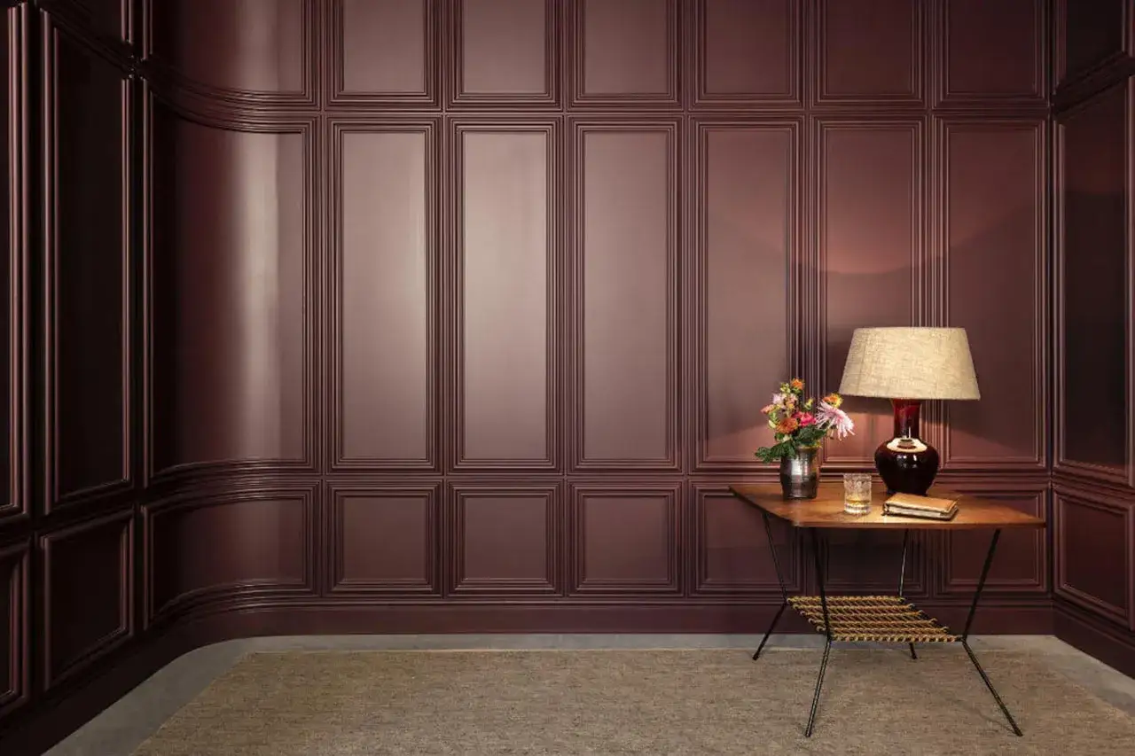 Elegancki montaż paneli ściennych PCV w odcieniu bordo. W rogu stoi stolik z lampą i bukietem kwiat&oacute;w.