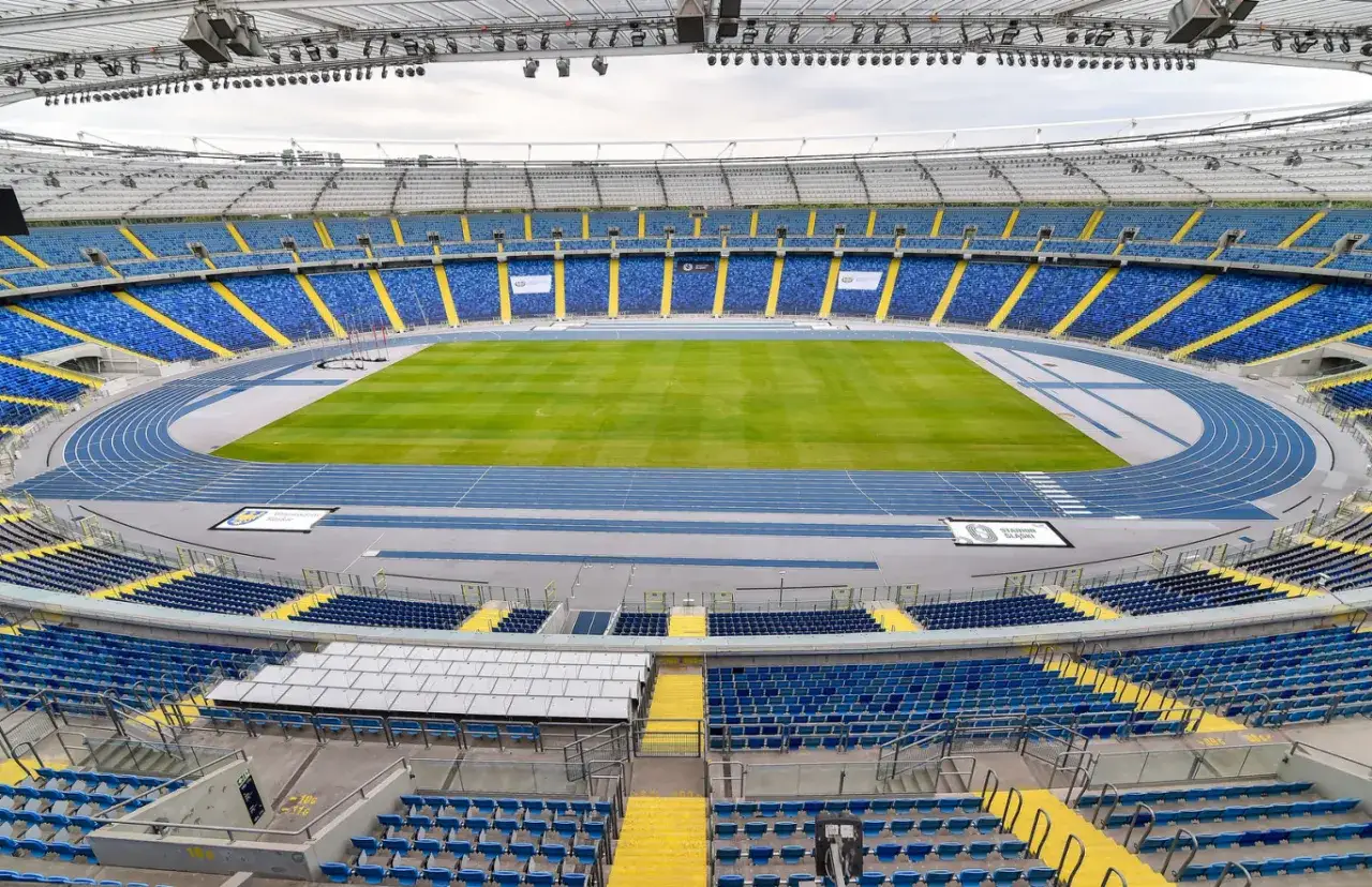 Widok na pusty Stadion Śląski w Chorzowie z niebieskimi trybunami i zieloną murawą.