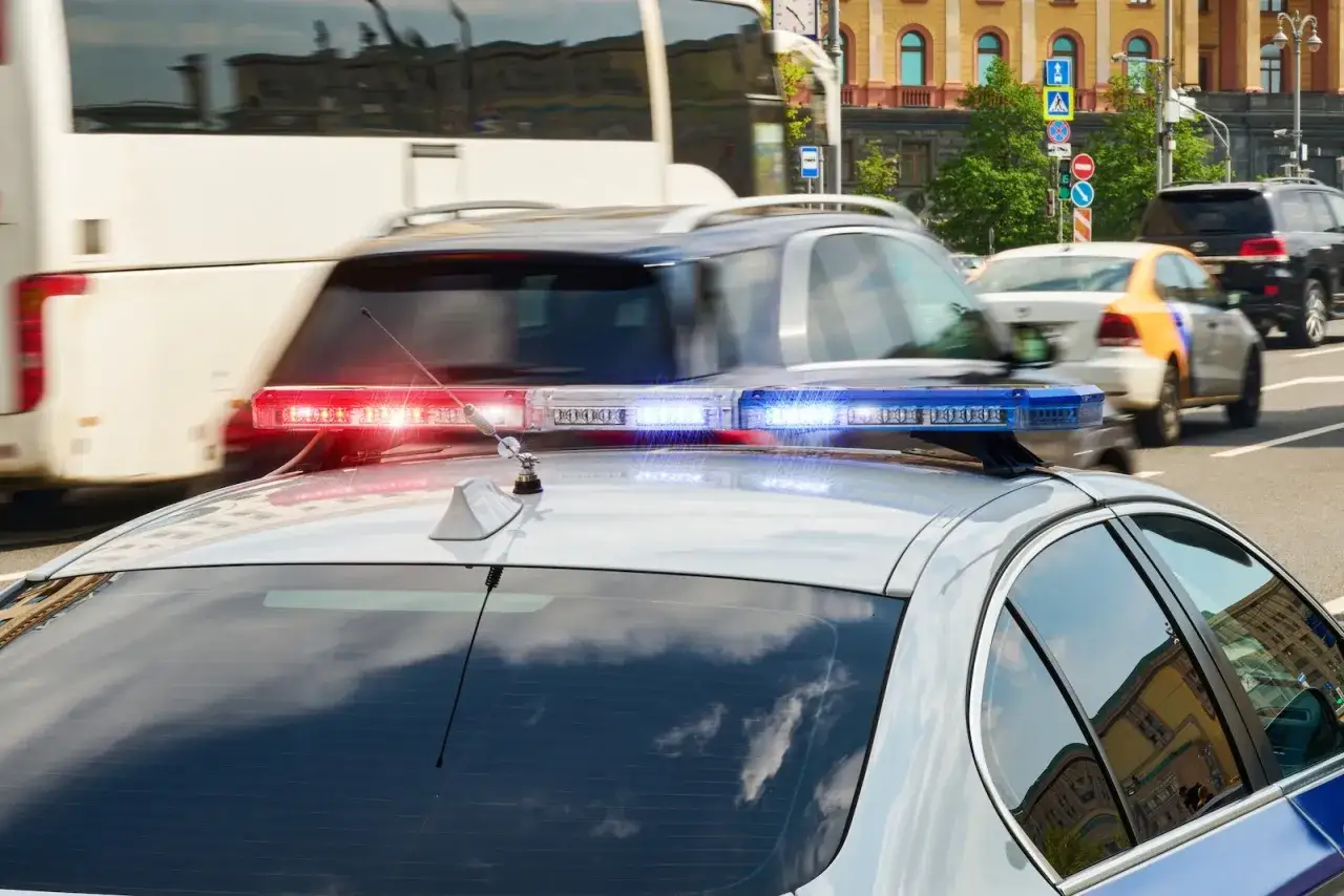 Policyjny radiowóz z włączonymi sygnałami świetlnymi. Pamiętaj, kiedy można wyprzedzać pojazd uprzywilejowany, aby zapewnić bezpieczeństwo.