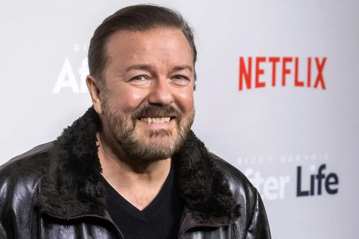 Ricky Gervais, znany z ciętego humoru i stand-upu, uśmiecha się na tle logo Netflix i napisu 