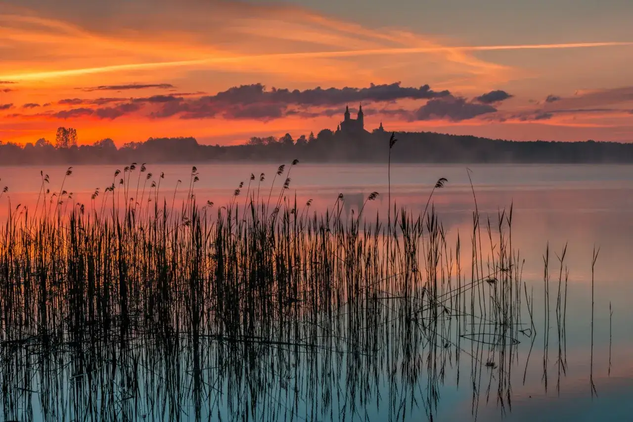 Mglisty poranek nad jeziorem, z widocznym w oddali kościołem na wzgórzu. Czy Polska ma jakieś wyspy? To miejsce wygląda jak z bajki, choć nie jest wyspą.