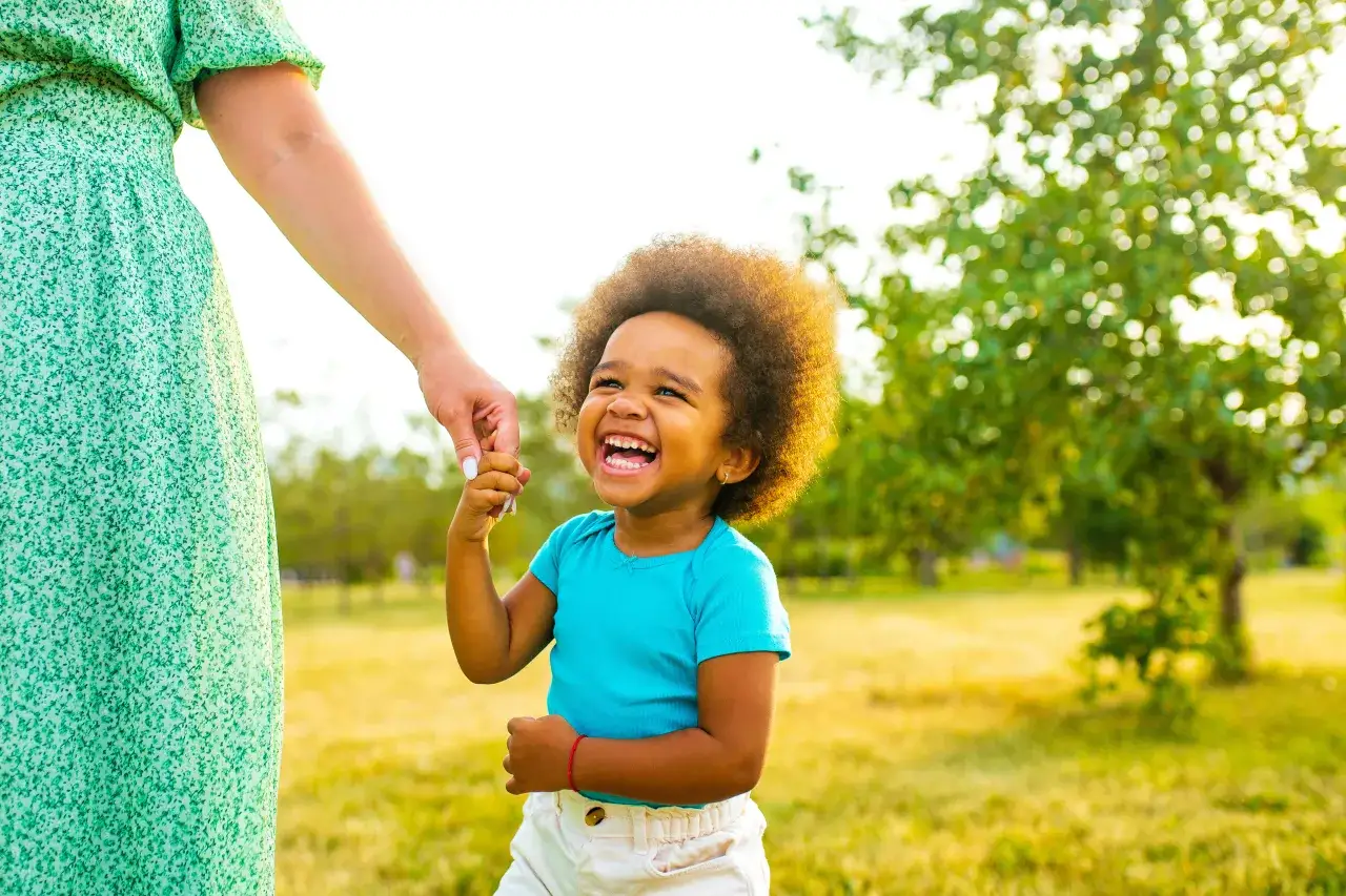 Szczęśliwe dziecko trzymające za rękę dorosłego na tle natury. Czy rodzina adopcyjna dostaje pieniądze? To pytanie nie ma znaczenia, gdy liczy się miłość.