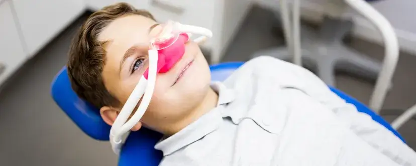 Dziecko z maseczką do gazu rozweselającego u dentysty, uśmiechnięte