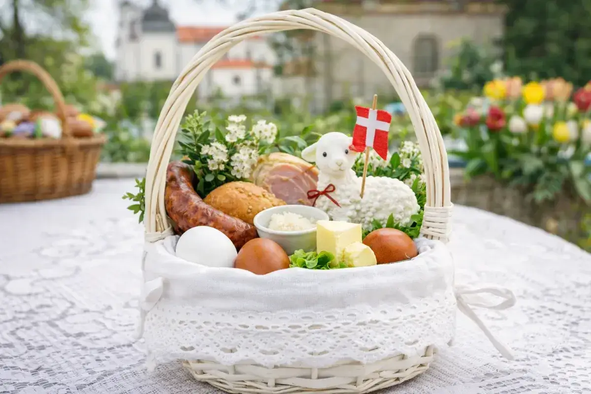 Biały koszyk z tradycyjnymi produktami do święconki: jajka, kiełbasa, chleb, masło, baranek z flagą Danii.