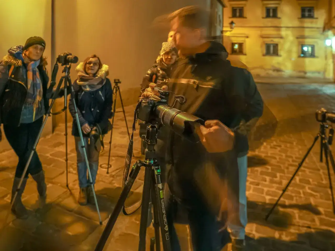 Uczestnicy szkolenia online dla fotograf&oacute;w ćwiczą nocne fotografowanie na ulicy, używając statyw&oacute;w i aparat&oacute;w.