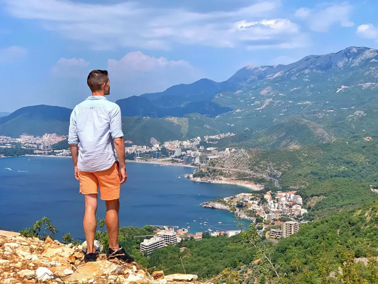 Mężczyzna na szczycie wzg&oacute;rza podziwia widok na wybrzeże Czarnog&oacute;ry. Czy czarnog&oacute;ra jest bezpieczna? Tak, wygląda na spokojną i piękną.