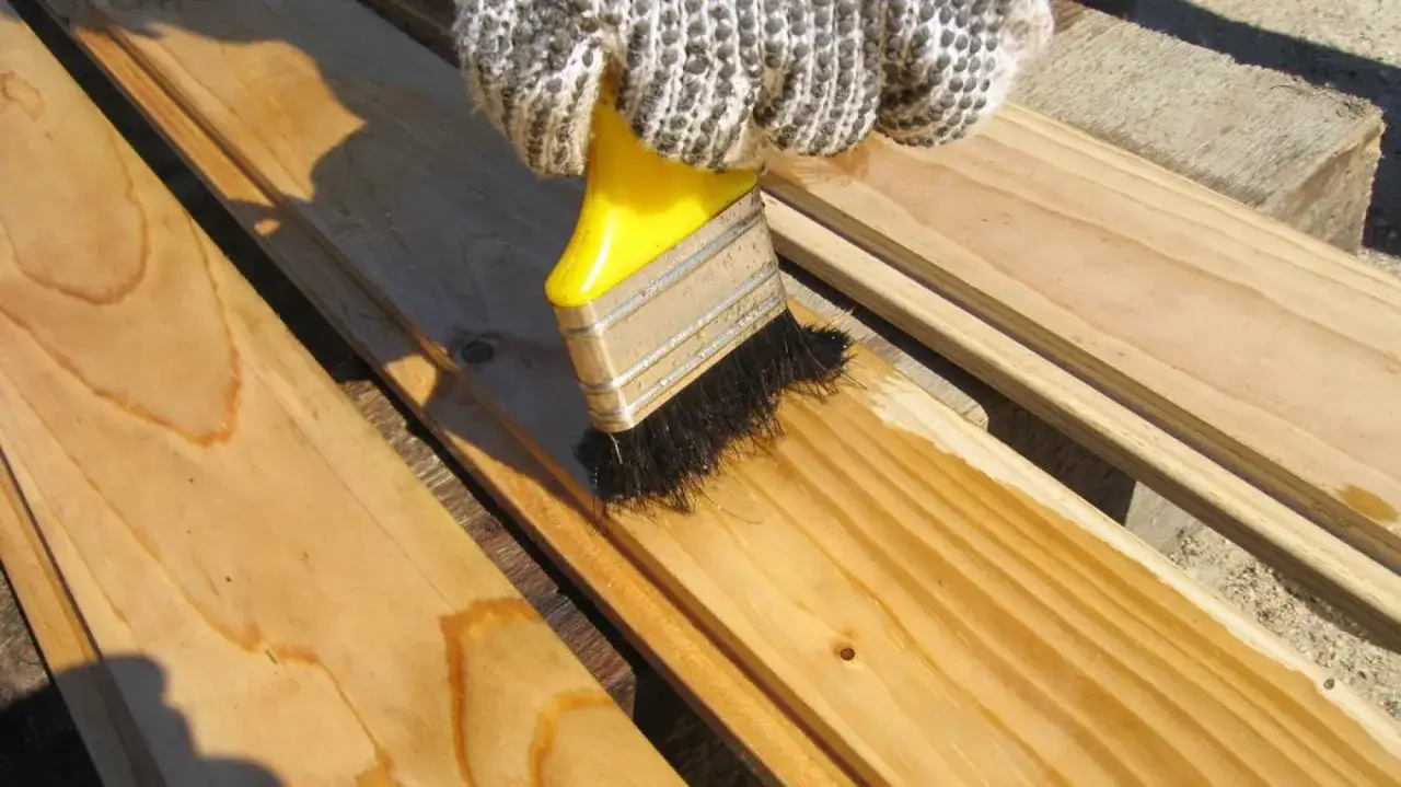 Rękawica w białej rękawiczce nakłada impregnat do drewna natryskowy na deski.