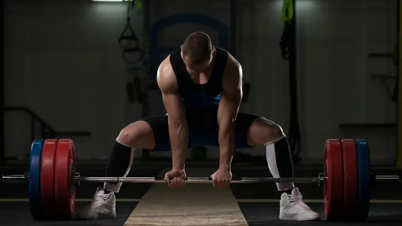 Siłacz w pozycji do martwego ciągu sumo, z szeroko rozstawionymi nogami i sztangą.