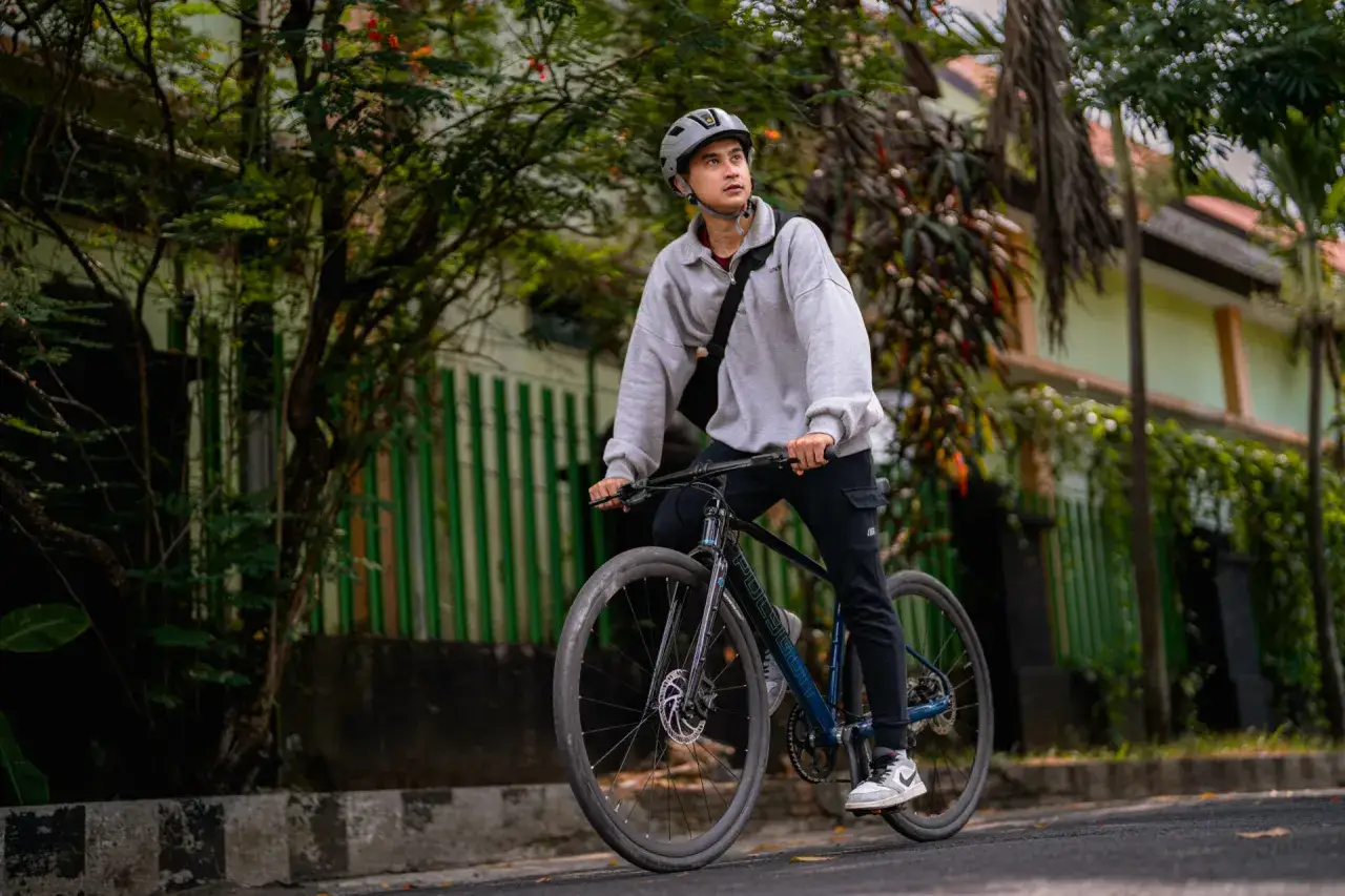 Młody mężczyzna w kasku jedzie na rowerze, zastanawiając się, czy jazda na rowerze odchudza. W tle zielona roślinność i dom.