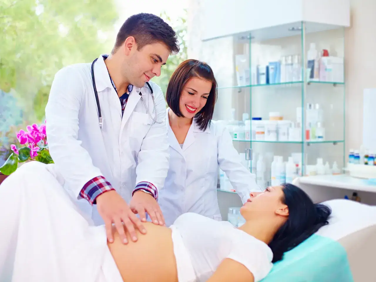 Lekarz i pielęgniarka badają brzuch ciężarnej kobiety. Może to być przygotowanie do porodu, np. lewatywa przed porodem.