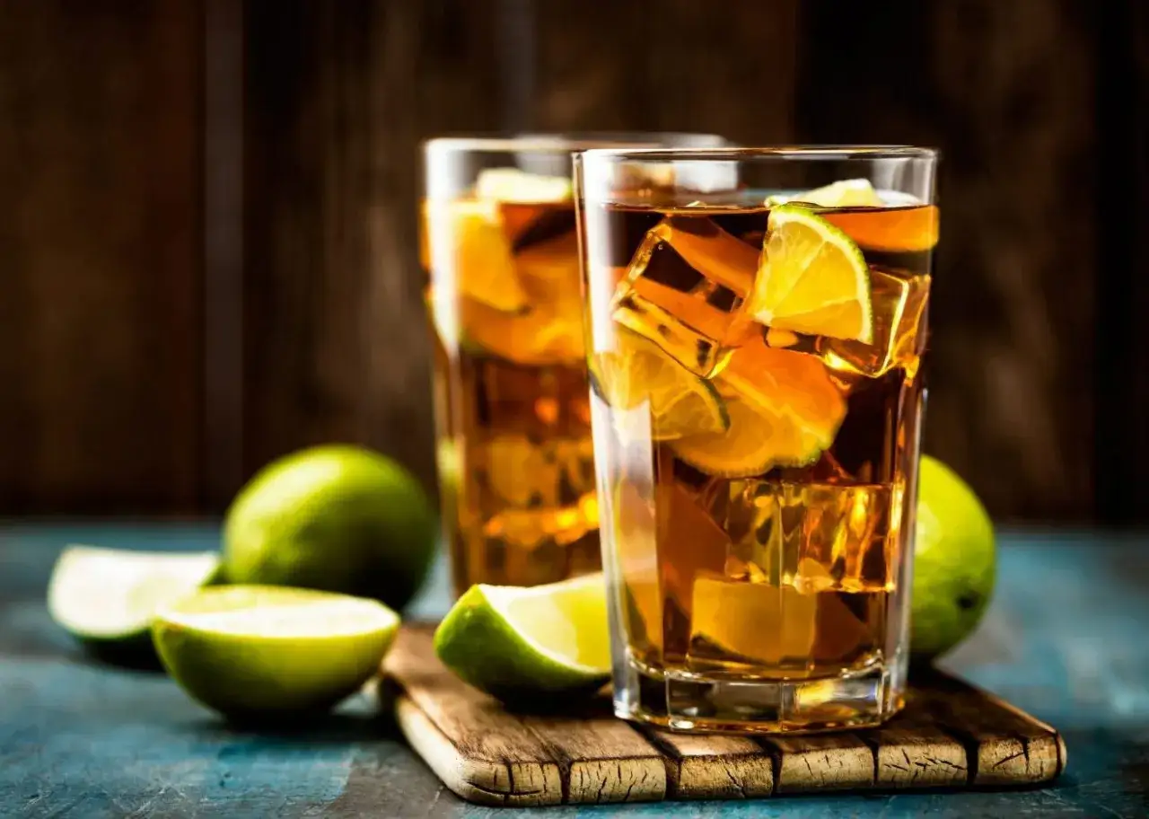 Dwa orzeźwiające drinki Long Island z lodem i plasterkami limonki, otoczone świeżymi owocami.