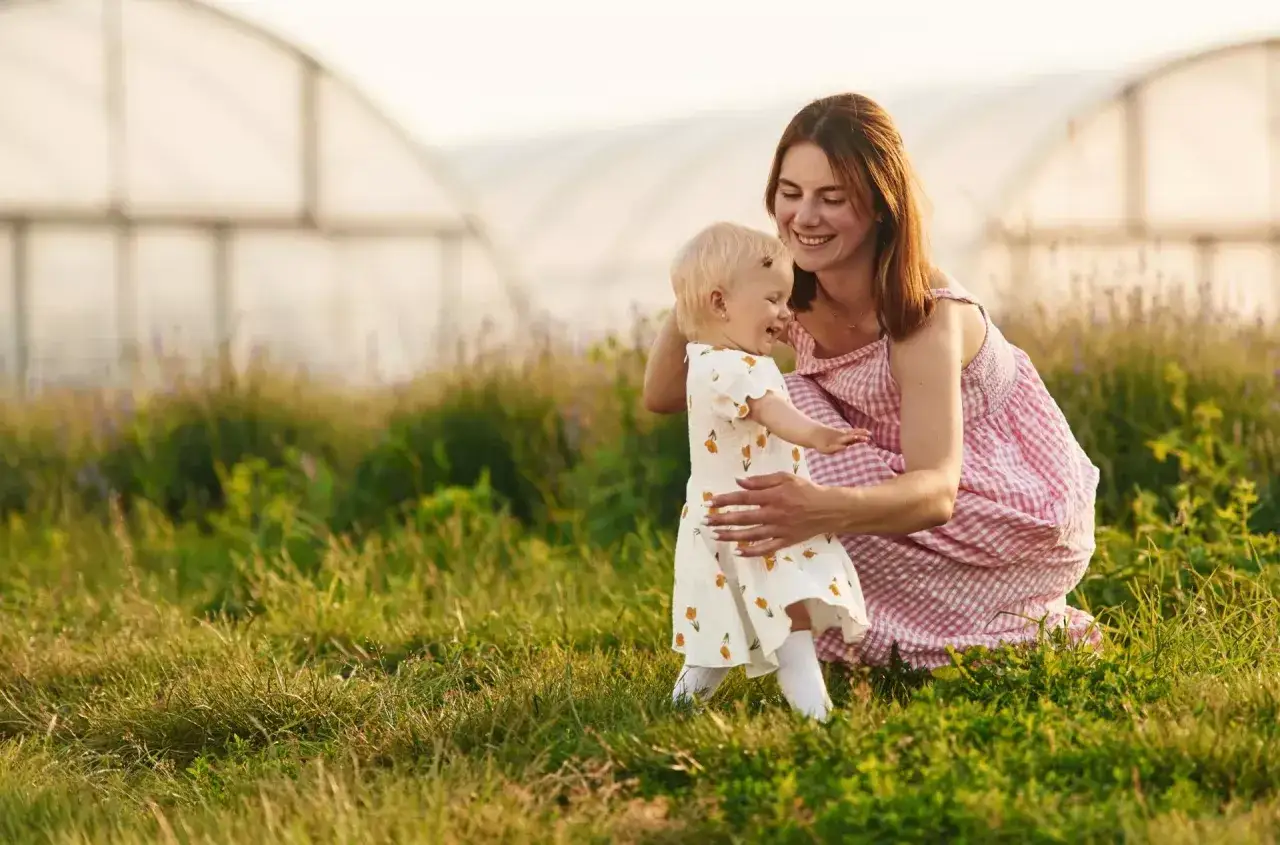Uśmiechnięta opiekunka bawi się z dzieckiem na łące. Zastanawiasz się, ile bierze opiekunka do dzieci za taką radość?