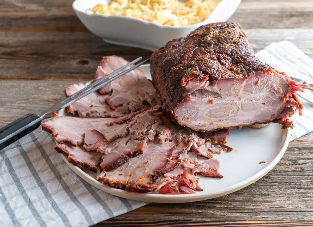 Pokrojona, soczysta karkówka pieczona, z przypieczoną skórką, na talerzu obok miski z surówką. Idealna na rodzinny obiad.